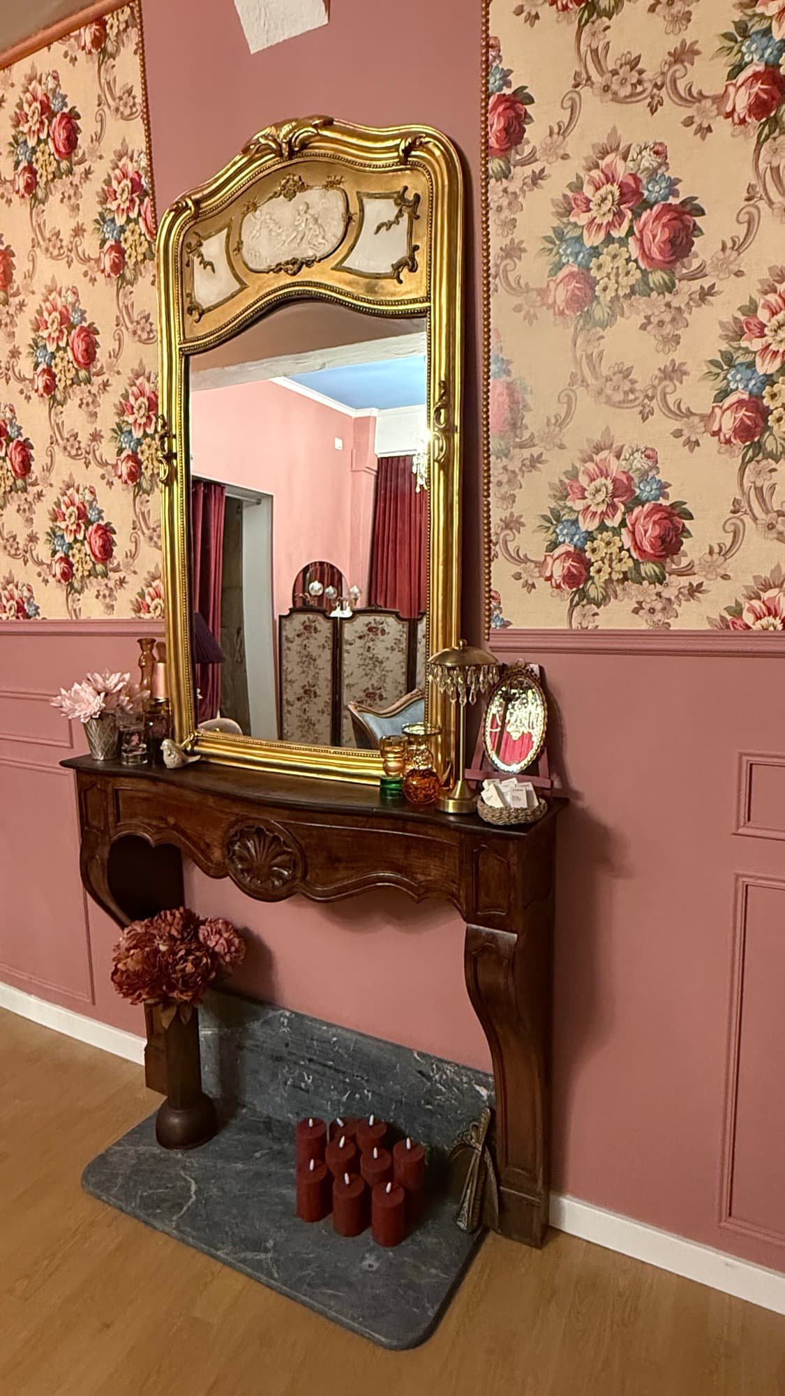 Cheminée en bois sculpté surmontée d'un grand miroir doré, papier peint fleuri